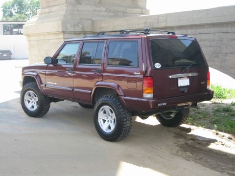 2000 Jeep Cherokee - This lifted Jeep Cherokee XJ is shown from a rear three-quarter angle, parked on a dirt and concrete surface.