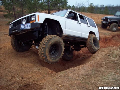 1986 Ford Bronco - A lifted Jeep Cherokee XJ navigates a challenging off-road trail, with another Jeep in the distance.