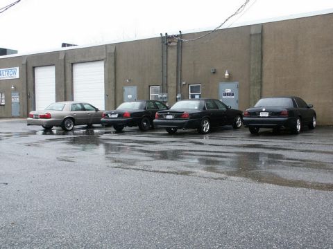 2001 Mercury Grand Marquis - Several sedans are parked in front of a commercial building on a wet day.