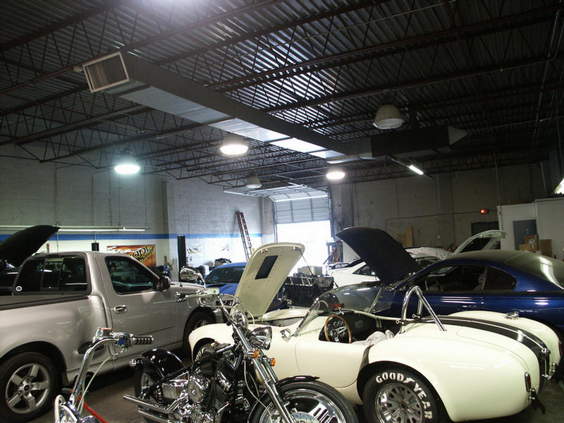 Auto shop interior with classic cars, a white Cobra roadster replica and motorcycles under hoods