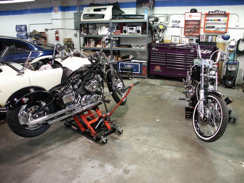 two motorcycles in a garage, one on a lift, with shelves and tools in background