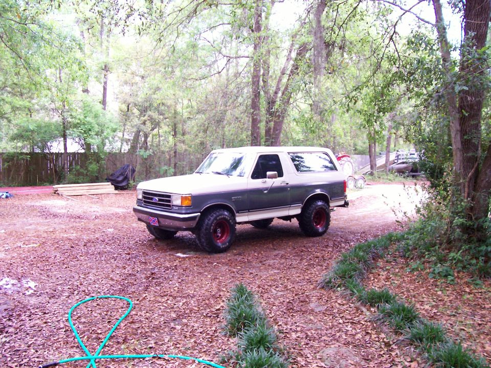 Two-tone gray and white Ford Bronco with red wheels parked on a gravel driveway