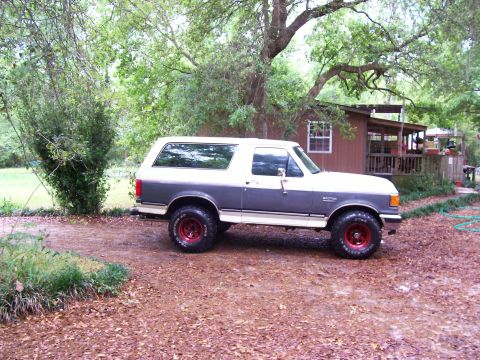1990 Ford Bronco - Side view of a two-tone 1990 Ford Bronco with red wheels parked outdoors.