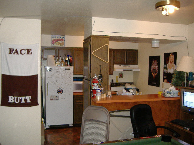 Interior view of a room with a refrigerator, kitchen counter, stove, and a computer monitor