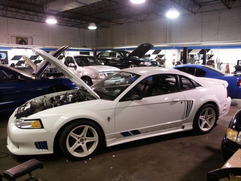 2001 Mercury Grand Marquis - A white Ford Mustang is parked inside a garage with its hood open, alongside other vehicles.
