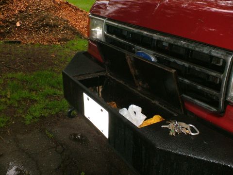 1989 Ford Bronco - Black textured-finish custom front bumper on a red Ford truck with the built-in storage compartment lid propped open, revealing a plastic b…