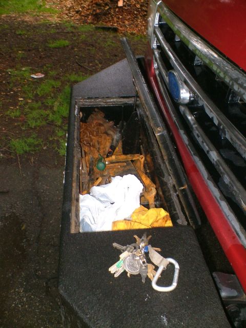1989 Ford Bronco - Looking down at a bed-liner-coated front bumper with a built-in storage compartment, its hinged lid open to reveal a rusty chain, a yellow…