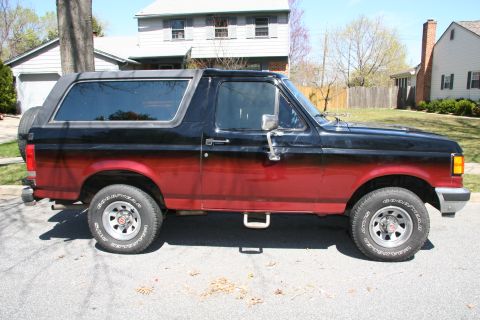 1990 Ford Bronco - A two-tone Ford Bronco is parked on a residential street with houses in the background.