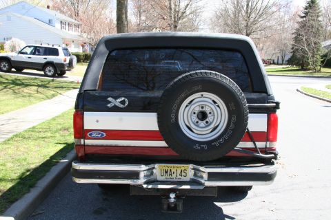 1990 Ford Bronco - This 1990 Ford Bronco features a rear-mounted spare tire and a distinctive red and white stripe pattern on its tailgate.