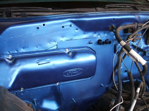 1974 Ford Ranchero - Close-up inside an engine bay showing a metallic-blue painted stamped steel valve cover with an embossed Ford oval, bolted to a matching bl…