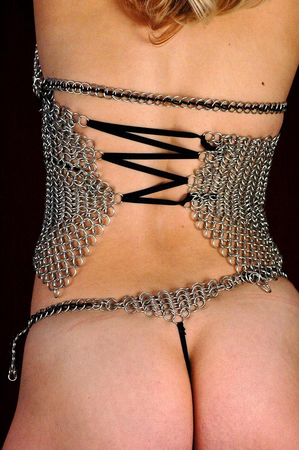 Person modeling a chainmail corset garment against a dark backdrop