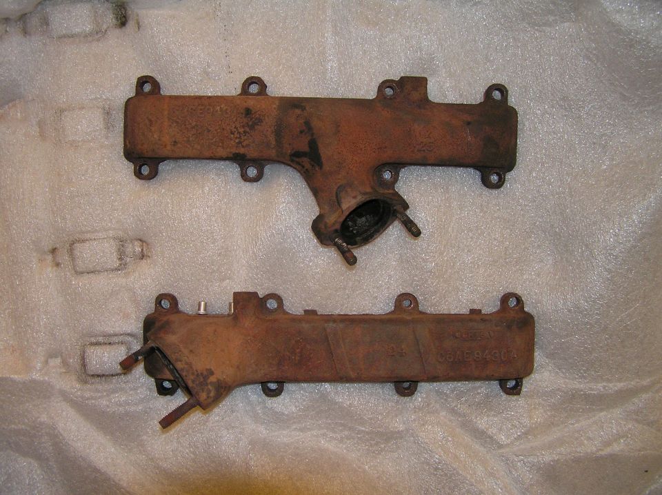 Pair of rusty cast-iron exhaust manifolds on white foam