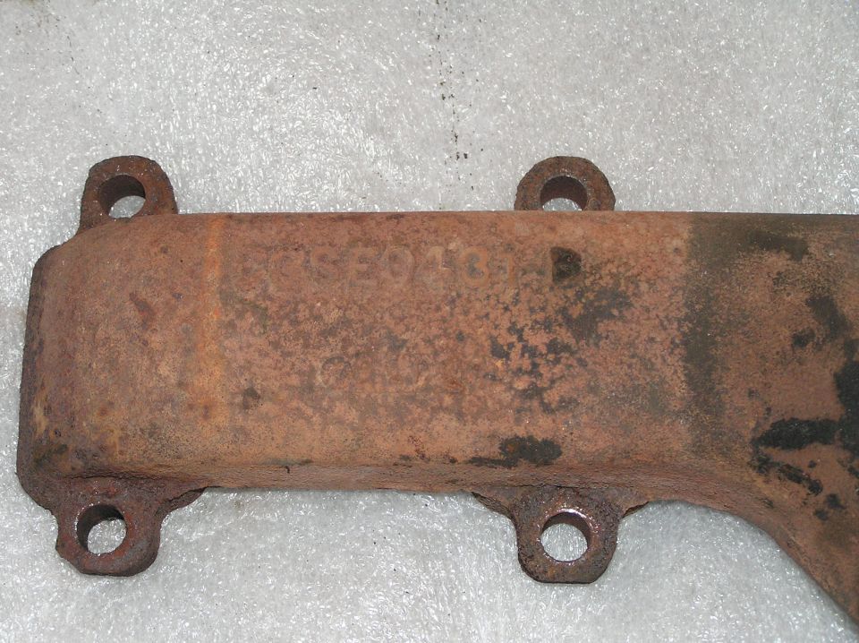 Rusty cast iron exhaust manifold with bolt holes and casting numbers