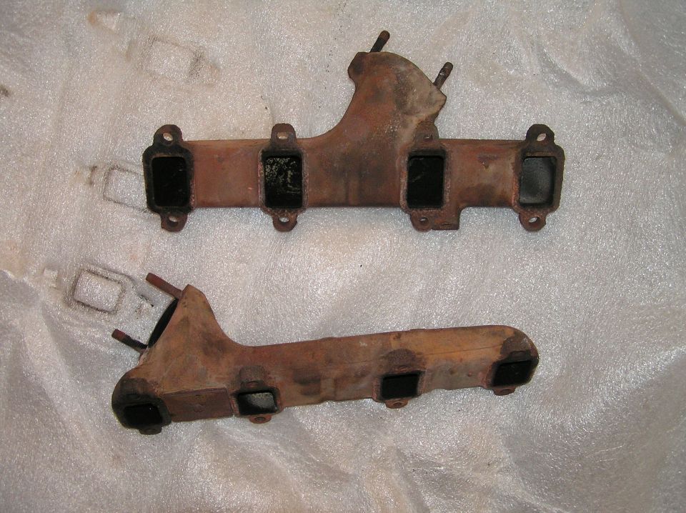 Two rusty cast-iron exhaust manifolds on white foam