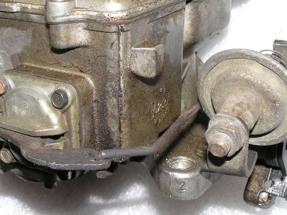 Dirty aluminum carburetor with linkage, bolts and diaphragm housing on white background