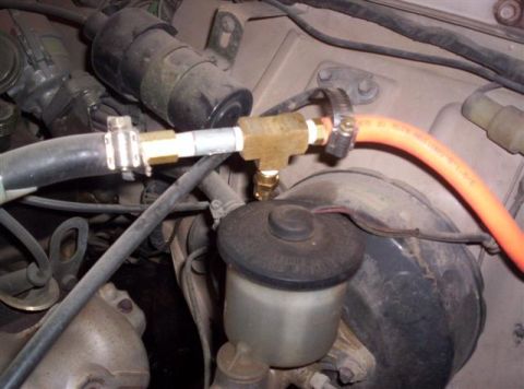 1987 Suzuki Samurai - Close-up of engine bay plumbing, including a T-fitting and brake fluid reservoir.