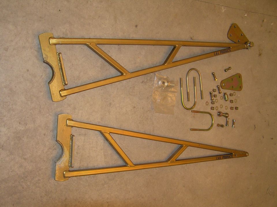 Pair of gold powder-coated triangulated traction/ladder bars with U-bolts and mounting hardware on the floor
