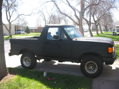 1991 Ford Bronco - A black 1991 Ford Bronco is parked on a residential street with trees and houses in the background.