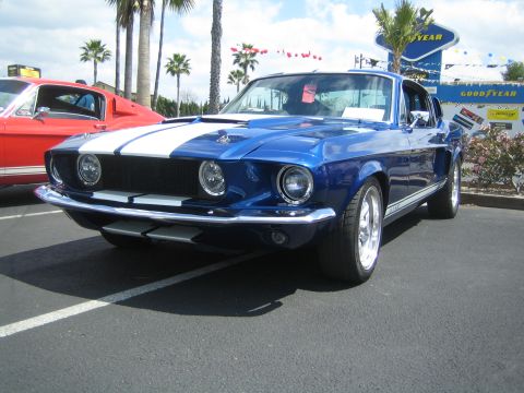 1968 Ford Mustang - A blue 1968 Ford Mustang with white racing stripes is parked at an outdoor event with a red car beside it.