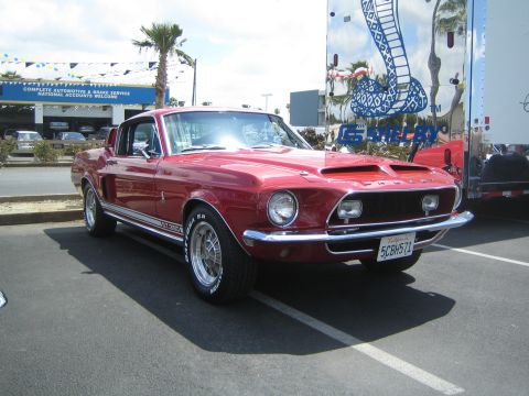 1968 Ford Mustang - A red 1968 Shelby GT500 Mustang is parked in a lot, with a large trailer a cobra graphic behind it.