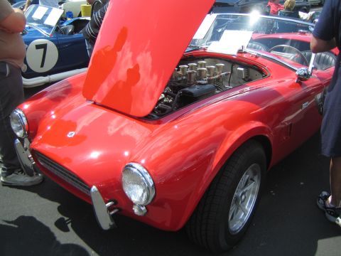 1968 Ford Mustang - A red sports car is displayed with its hood open, revealing the engine compartment. Another car is visible in the background.