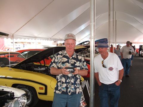 1966 Ford Ranchero - Men observe vehicles displayed under a tent at an outdoor event.