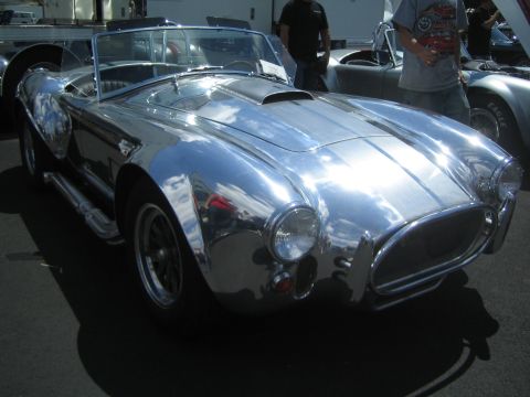 1968 Ford Mustang - A highly reflective chrome AC Cobra replica is displayed at an outdoor car show, with other vehicles visible in the background.