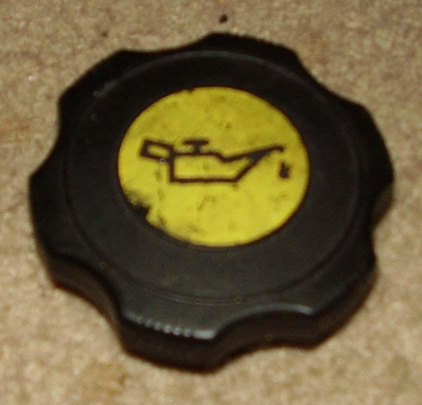 Black plastic oil filler cap with yellow oilcan symbol on carpet