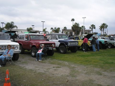 1966 Ford Bronco - A row of early Ford Broncos lined up on grass at an outdoor club show, including white, maroon, dark blue with a 'So Cal Broncos' windshiel…
