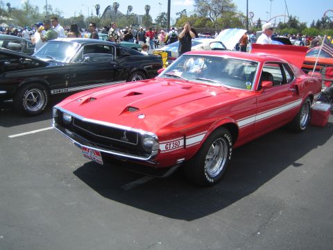 1968 Ford Mustang - A red 1969 Ford Mustang GT350 is displayed at an outdoor car show with other vehicles present.