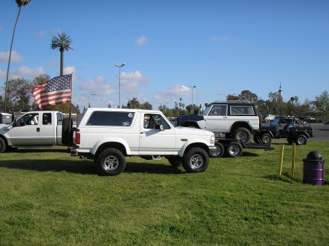 1966 Ford Bronco - Side profile of a lifted white 1990s full-size Ford Bronco on polished alloy wheels and mud tires, parked on grass at an outdoor show next…