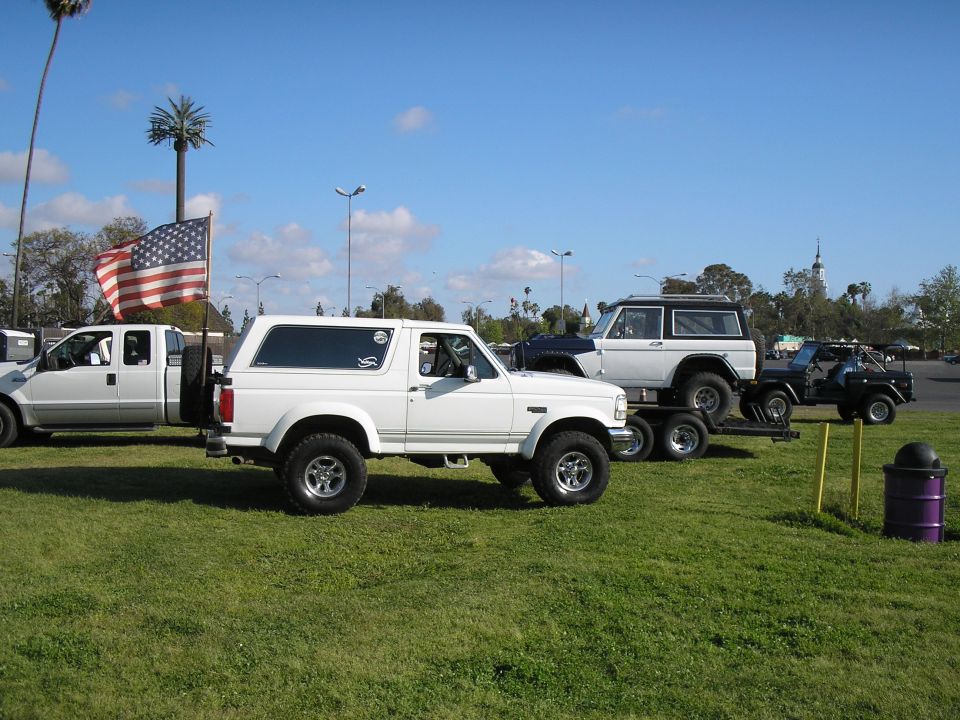 Lifted white 1990s Ford Bronco side view at outdoor show with flag-flying pickup