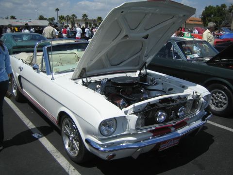 1968 Ford Mustang - A white 1965 Ford Mustang convertible is displayed with its hood open, revealing the engine bay.