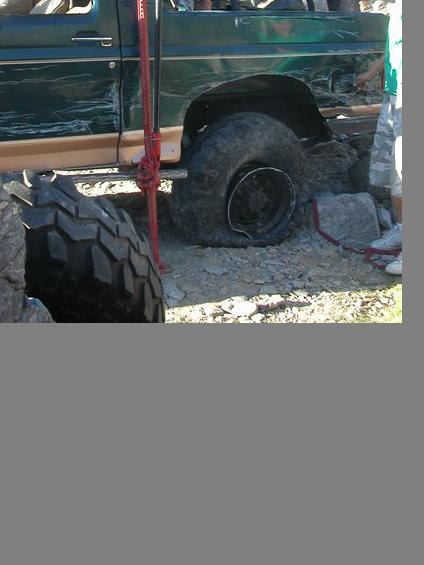 1990 Ford Bronco - A green Ford Bronco with a flat tire is being lifted by a red jack, suggesting it is stuck or undergoing maintenance.