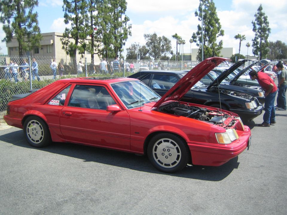 Red 1987 Ford Mustang coupe, hood open, parked in a line with other cars