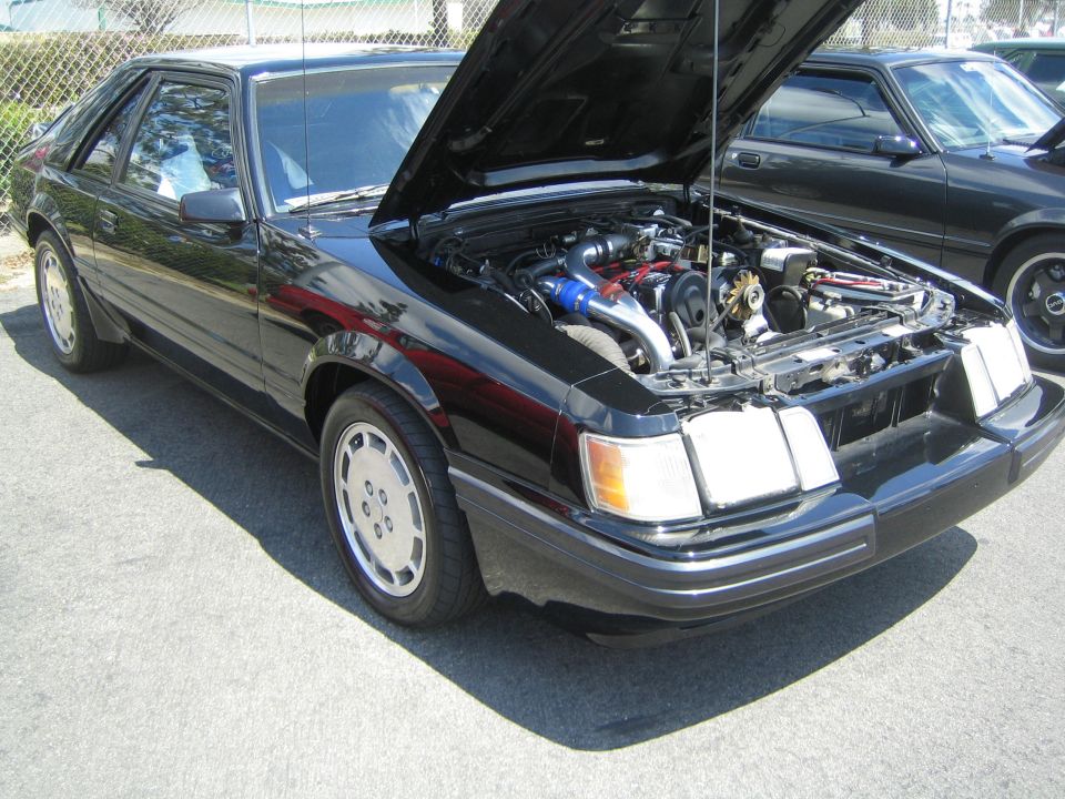 Black Fox body Ford Mustang with hood open, showing engine. Another Mustang is parked behind it