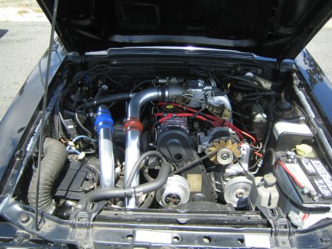 1968 Ford Mustang - The engine bay of a car is shown with a turbocharger and associated piping, along with red spark plug wires.
