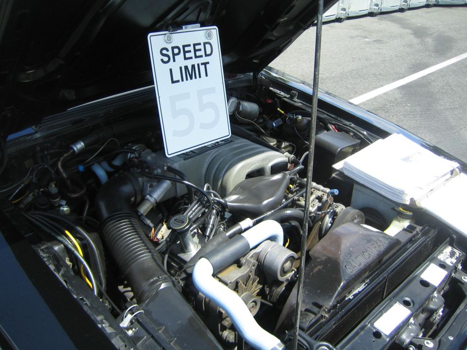 Engine bay of a car with a 'SPEED LIMIT 55' sign attached to the hood