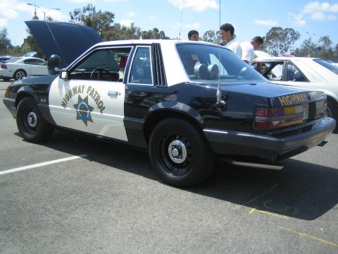 1968 Ford Mustang - A black and white police car is parked outside with its hood up.