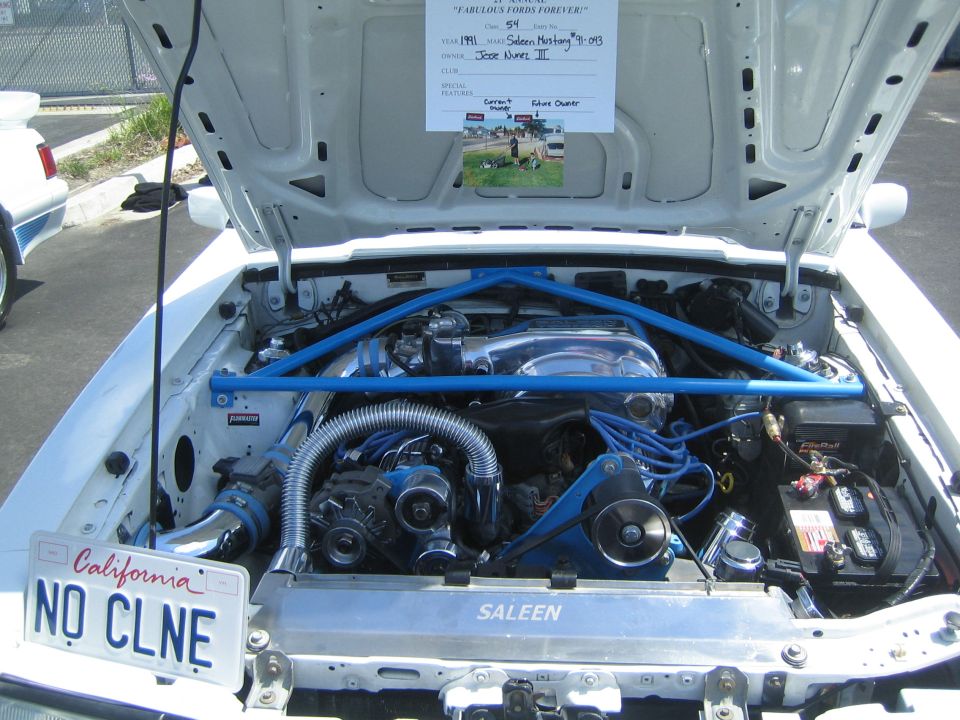 Engine bay of a Saleen Mustang with blue strut tower brace and chrome accents. California license plate reads 'NO CLNE'