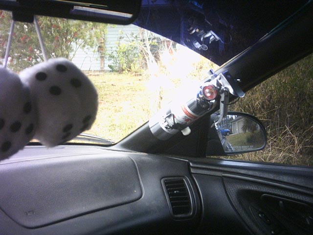 Car interior with fuzzy dice hanging from the rearview mirror and a fire extinguisher mounted on the windshield pillar