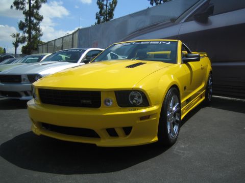 1968 Ford Mustang - A yellow convertible is parked in front of a large mural of a car.