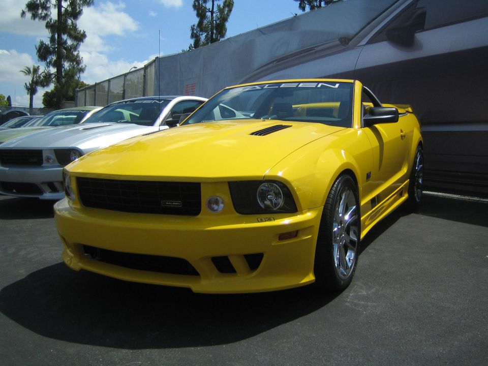 Yellow convertible with black racing stripes on the side and a 'Saleen' banner on the windshield