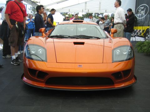1968 Ford Mustang - An orange sports car is displayed at an outdoor event, with spectators gathered around.