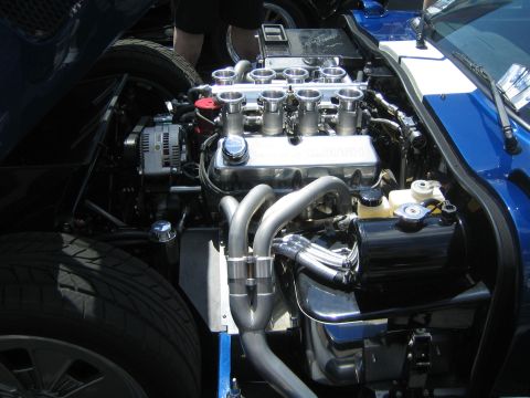 1968 Ford Mustang - The engine bay of a blue car, a V8 engine with custom chrome components and exhaust system.