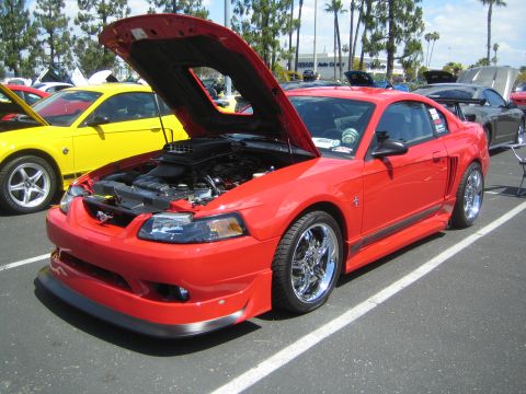 1968 Ford Mustang - A red Ford Mustang is displayed with its hood open at an outdoor car show, alongside other vehicles.
