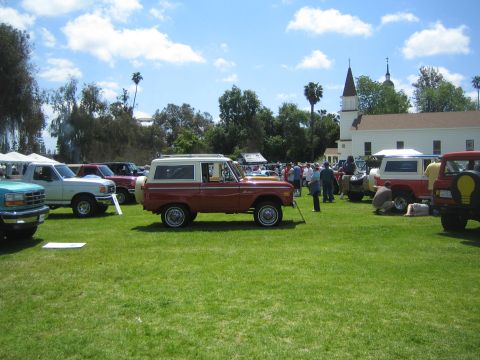 1968 Ford Mustang - A collection of vehicles, including a red and white Ford Bronco, displayed on a grassy field under a partly cloudy sky.