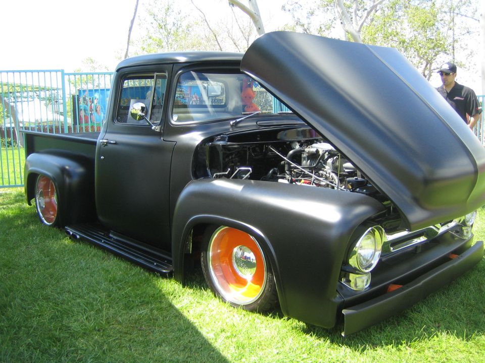 Matte black 1956 Ford F-100 pickup truck with orange-rimmed wheels and hood open