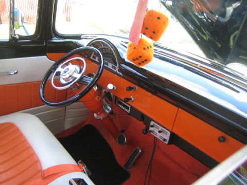 1968 Ford Mustang - The interior of a classic car features orange and white upholstery and fuzzy dice hanging from the mirror.