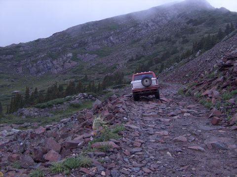 1978 Ford Bronco - A 1978 Ford Bronco navigates a challenging, rocky mountain path under a cloudy sky.